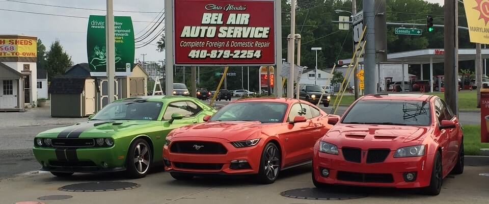 Three cars in front of the Bel Air Auto Service sign: a lime green Roadrunner with black racing stripes, a fire engine red Ford Mustang GT, and a deep red Pontiac GTO.